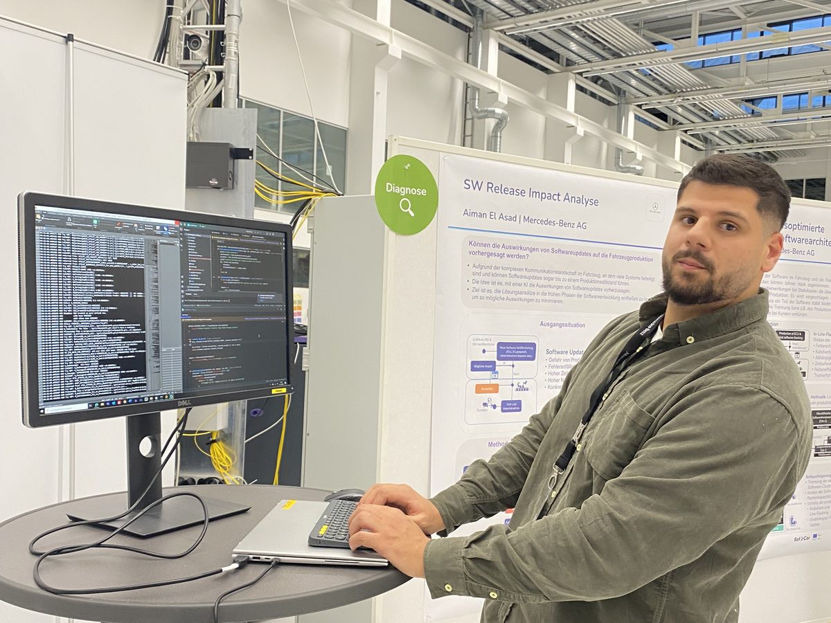 Aiman El Asad at a standing desk next to his poster on software release impact analysis